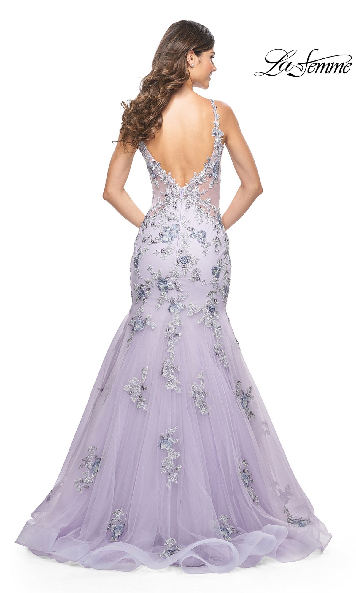 A woman models the La Femme Long Lavender Mermaid Prom Dress 32091, featuring a low back and floral appliqués, as she stands with her back to the camera. The